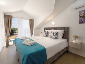 Ein Hotelzimmer mit Bett, Nachttisch, Lampe, einem Gemälde und Blick ins Freie.