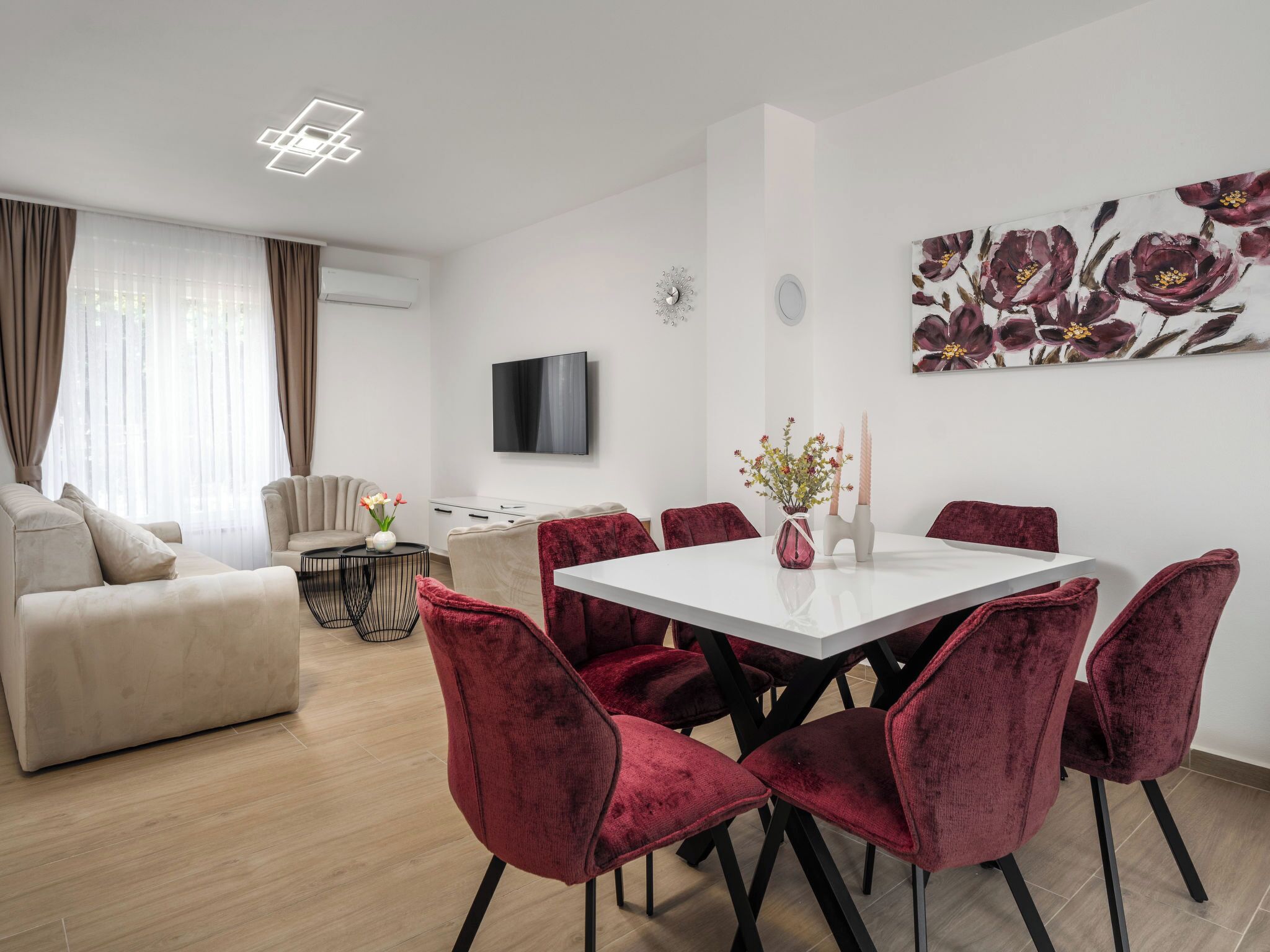 En moderne stue med en sofa, et spisebord med stole, et fjernsyn og et blomsterbillede på væggen.