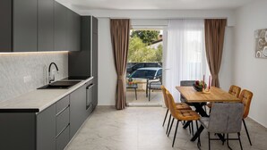 A modern kitchen with grey cabinets, a black sink, and a dining area with a wooden table and chairs. - Mediterranee Oliva by Interhome (Poreč/Funtana)