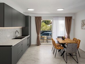 A modern kitchen with grey cabinets, a black sink, and a dining area with a wooden table and chairs. - Mediterranee Oliva by Interhome (Poreč/Funtana)