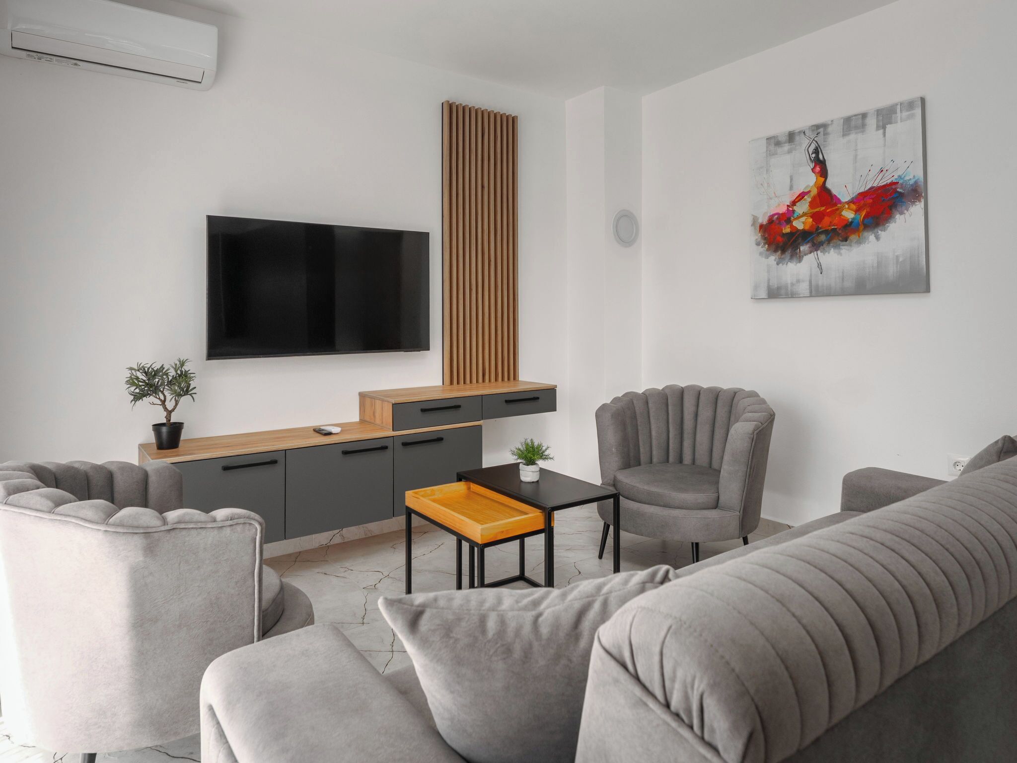 Una sala de estar moderna con un televisor de pantalla plana, un mueble de madera, sofás grises, una mesita y un cuadro en la pared.