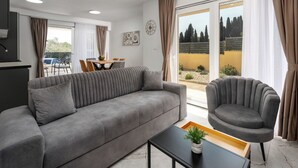 A modern living room with a sofa, armchair, dining table, and a view of the outdoors. - Mediterranee Oliva by Interhome (Poreč/Funtana)