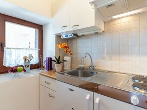 A kitchen with a sink, stove, cabinets, and a window with a curtain. - Apartment Orbani by Interhome (Lovran)