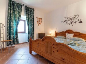 Un dormitorio con una cama de madera, una silla, un radiador, una luz fijada en la pared y una ventana con cortinas.