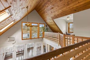 A loft-style room with a wooden ceiling, a balcony with a wooden railing, and a large window with a view of trees. - Impressive, 4 Bedroom Waterfront Home, King Suite (Weare)