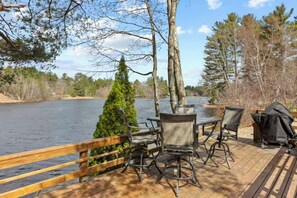 A deck with outdoor seating and a grill, overlooking a lake with trees in the background. - Impressive, 4 Bedroom Waterfront Home, King Suite (Weare)