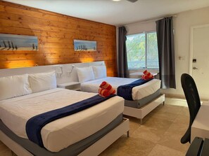 Ein Hotelzimmer mit zwei Betten, Holzwandverkleidung, einem Fenster mit Vorhängen und einem Schreibtisch mit Stuhl.