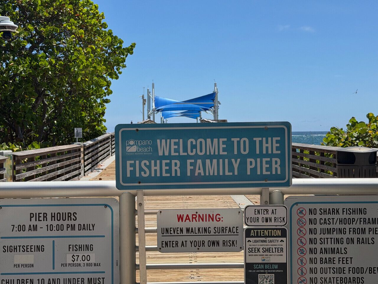 Un cartel da la bienvenida a los visitantes al Muelle Fisher, con horarios de apertura, tarifas y advertencias de seguridad.