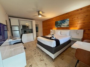 A modern hotel room with a bed, desk, chair, and a wooden wall. - Modern Cozy Beach Studio #17 (Pompano Beach)