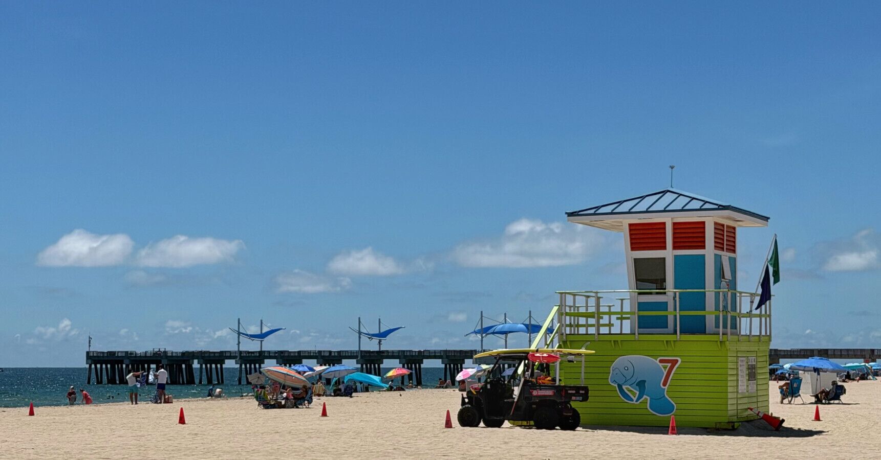 Une tour de surveillance avec une décoration aux couleurs bleu et vert, une jetée avec des parasols bleus et des chaises de plage.