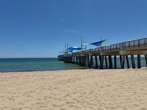 A beach with a pier extending into the water, featuring a covered walkway and a railing. - Bright Coastal 2BR Apartment #10 (Pompano Beach)