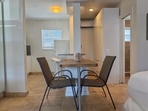 A hotel room with a bed, a dining table with chairs, a window, and a door. - Comfortable Studio • 5-Min Walk to Beach #15 (Pompano Beach)