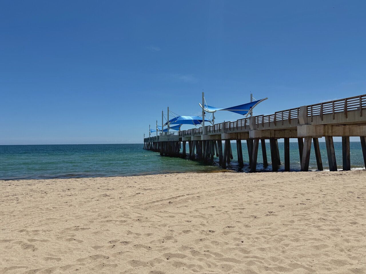 Una playa con un muelle que se adentra en el agua, con un paseo techado y una barandilla.