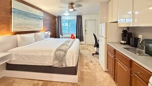A modern hotel room with a large bed, a kitchenette, a dining area, and a view of the city. - Bright & Cozy Studio #7 (Pompano Beach)