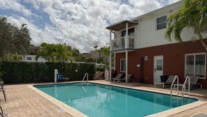 Piscina retangular com deck ladrilhado, um pequeno escorregador e cadeiras de descanso.