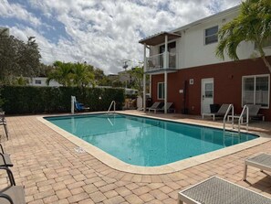 Una piscina rectangular con un borde de baldosas, un tobogán pequeño y sillas de descanso.