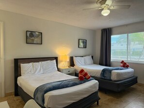 A hotel room with two beds, a ceiling fan, a window with curtains, and artwork on the walls. - Sunny Studio by the Pool • Near Beach & Dining #6 (Pompano Beach)