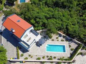 Vista aérea de uma casa moderna com telhado vermelho, piscina e jardim.