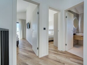 Een moderne hotelkamer met een houten vloer, een bed, een televisie en een badkamer met spiegel en wastafel.