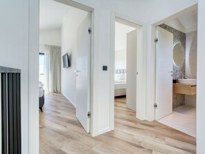 A modern hotel room with a wooden floor, a bed, a TV, and a bathroom with a sink and mirror. - Vacation home Dream by Interhome (Krk/Dobrinj)