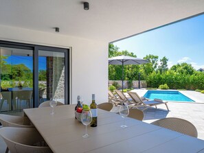An outdoor dining area with a pool, lounge chairs, and a table set with wine glasses and bottles. - Vacation home Dream by Interhome (Krk/Dobrinj)