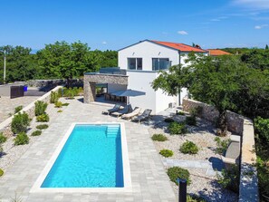 Uma casa moderna com piscina, paredes de pedra e um pátio com espreguiçadeiras.