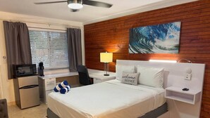 Een hotelkamer met een bed, bureau, koelkast, lamp en een schilderij aan de muur.