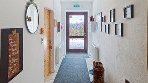 Ein Flur mit einer Holztür, einem Spiegel, gerahmten Bildern und Blick auf Berge durch eine Tür.