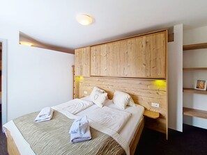 A bedroom with a wooden headboard, a bed with white linens, a bedside table, and a shelf with a picture frame. - Naviser Hütte by Interhome (Navis)