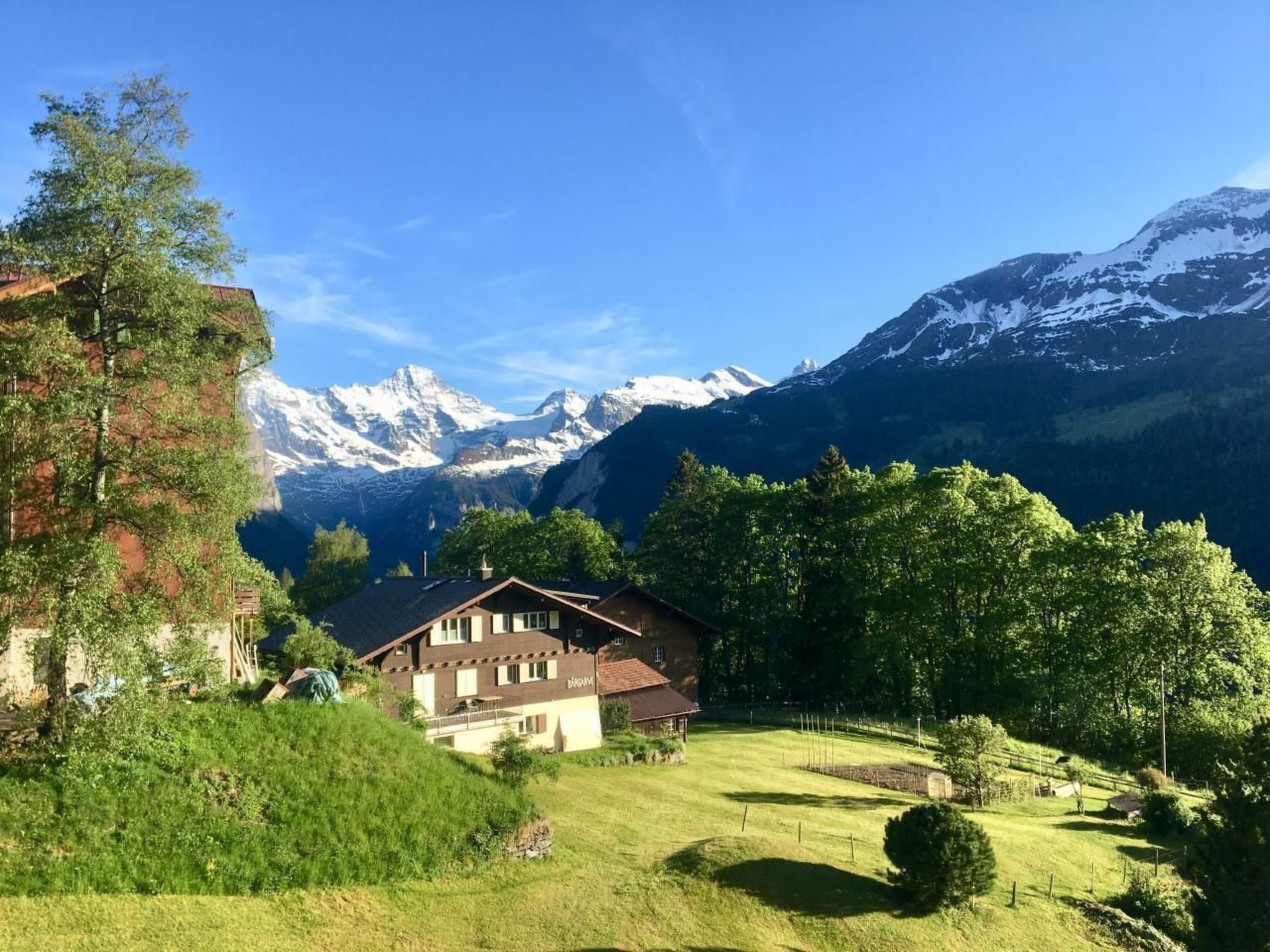 A chalet with a mountain view, surrounded by greenery and a clear sky.