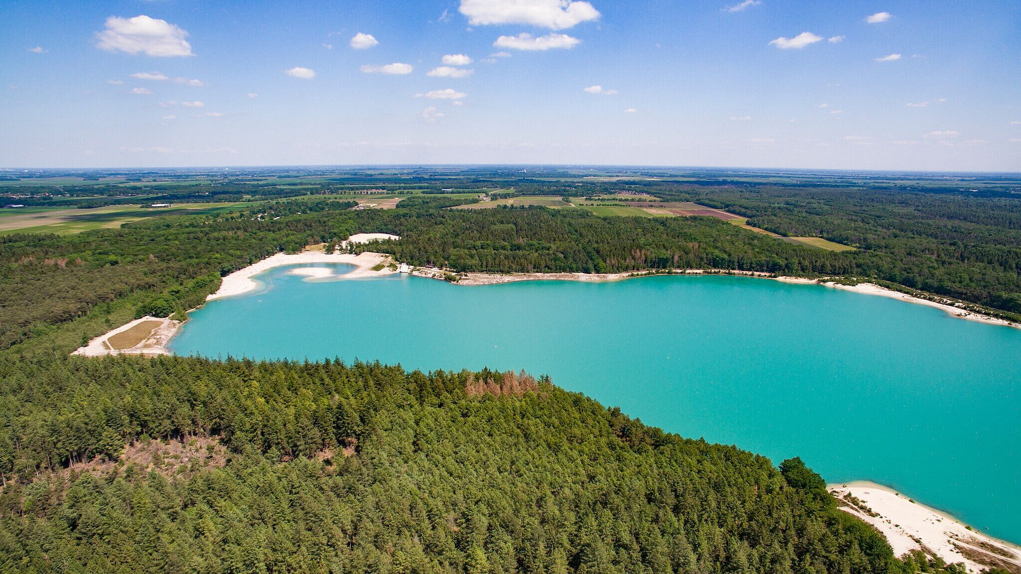 Een luchtbeeld van een groot, turquoise meer, omgeven door dichte bossen.