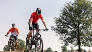Dos ciclistas en un sendero de tierra con árboles al fondo.