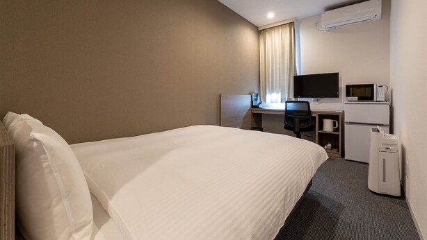 Une chambre d’hôtel équipée d’un lit, d’un bureau avec un ordinateur, d’une télévision et d’un four à micro-ondes.