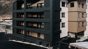 Un immeuble à plusieurs étages, doté de balcons et d’un toit plat, avec une chaîne de montagnes en arrière-plan.