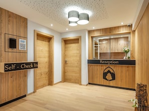 Ein Empfangsbereich mit Holzwänden, einem Schild für Self-Check-in, einem Empfangstresen und einer Decke mit einem perforierten Muster.