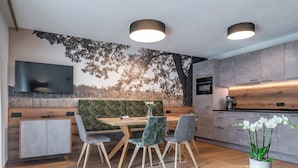 Ein moderner Essbereich mit Holztisch und -stühlen, einer großen Wandmalerei und einer Küche mit grauen Schränken.