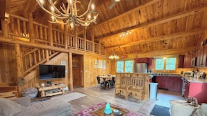 A log cabin interior with a living room, dining area, kitchen, and a staircase. - 7SD Cozy Log Cabin near Bretton Woods with Hot Tub, Firepit, Private Year (Twin Mountain)