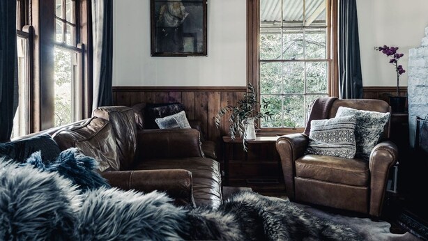 A cozy living room with a leather sofa, a chair, a fur throw, and a window with a view of trees. - Rosey Knoll Cottage ~ Cottage with delights of modern life (Daylesford)