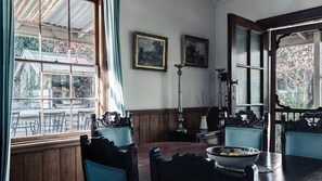 A dining room with a wooden table, chairs, and a vase with flowers. There are two framed paintings on the wall. - Rosey Knoll Cottage ~ Cottage with delights of modern life (Daylesford)