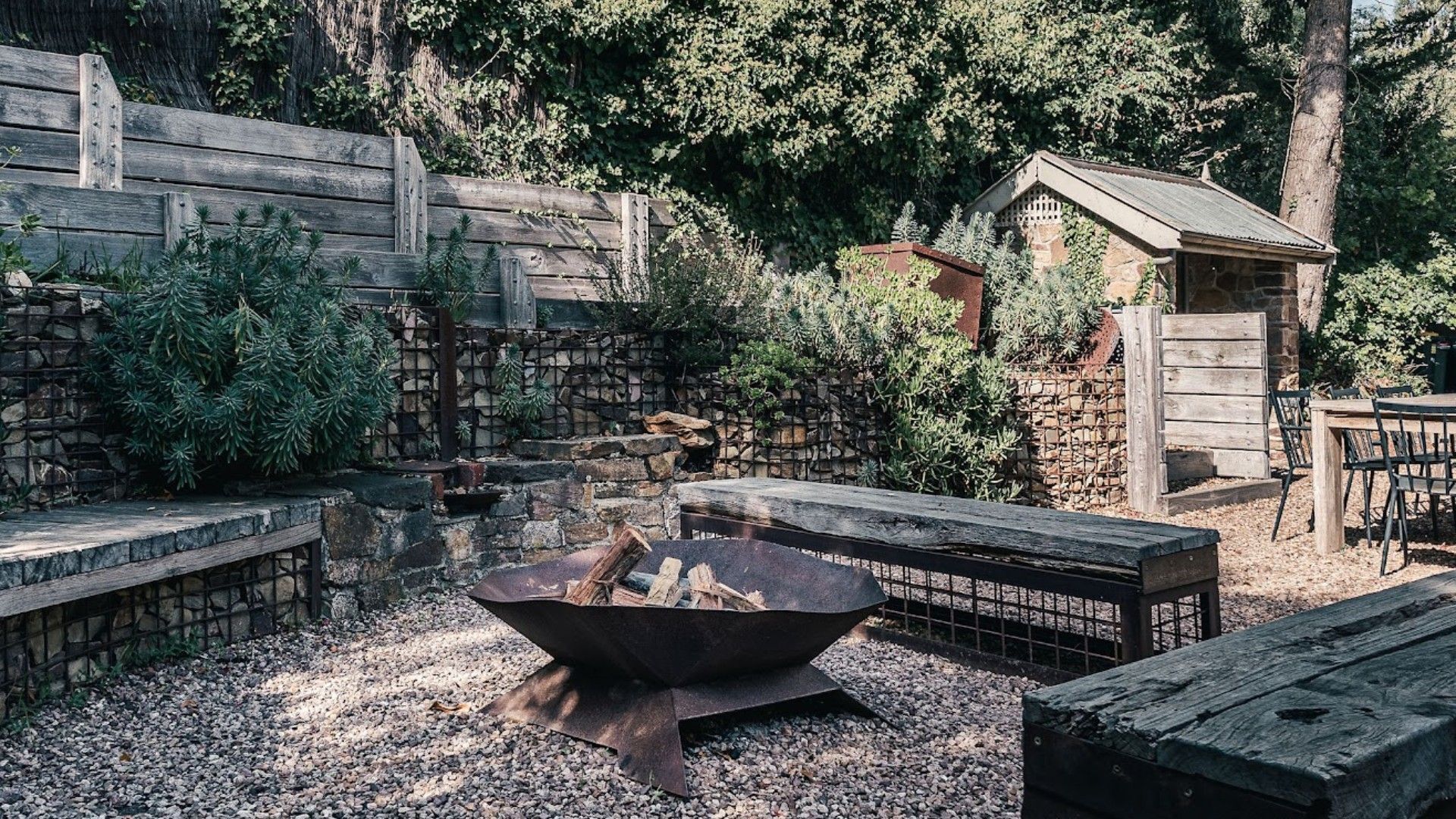 A rustic outdoor area with a fire pit, wooden benches, and a stone wall.