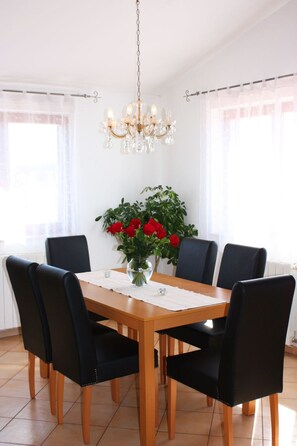 A dining room with a wooden table, black chairs, a chandelier, and a potted plant with red flowers. - Große Wohnung in Pješčana Uvala mit Eigenem Balk by Interhome (Pula/Banjole)