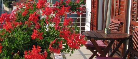 A balcony with red flowers, wooden furniture, and a white railing.