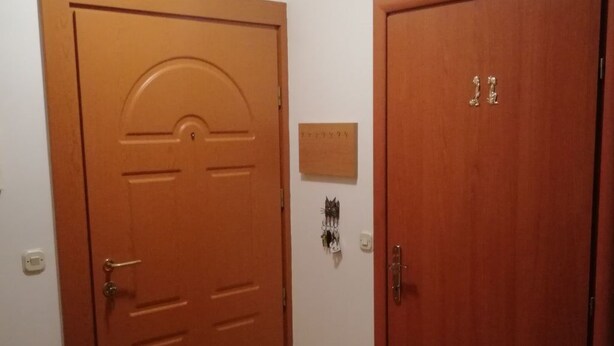Käytävä, jossa on kaksi puuovea, seinään kiinnitetty valaisin ja pieni laatta.