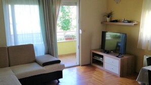 Olohuone, jossa on sohva, televisio, puulattia ja parveke, jossa on verhot.