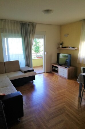 A living room with a sofa, TV, wooden flooring, and a balcony with curtains. - Zentrale Ferienwohnung mit überdachtem Balkon by Interhome (Crno)