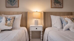 Une chambre d’hôtel avec deux lits, chacun agrémenté d’un coussin en forme d’étoile de mer, une table de chevet avec une lampe et deux œuvres d’art encadrées accrochées au mur.