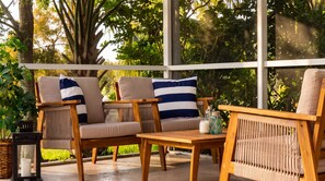 Un espace extérieur aménagé, abrité et doté de mobilier en bois et de coussins, entouré de verdure.