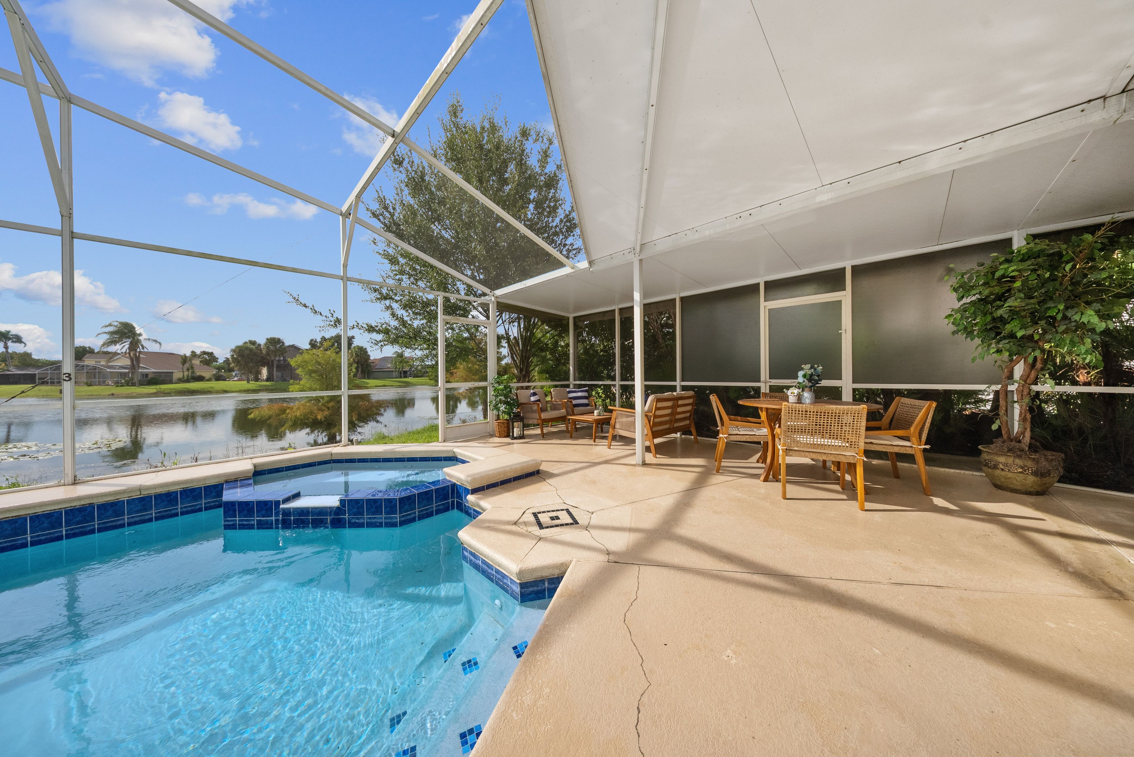 A pool area with a clear view of a lake, outdoor furniture, and a covered patio.