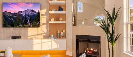 A modern living room with a fireplace, a television mounted on the wall, and a large window.