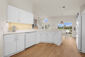Une cuisine moderne avec des meubles blancs, un lave-vaisselle encastré et une grande fenêtre donnant sur une piscine.